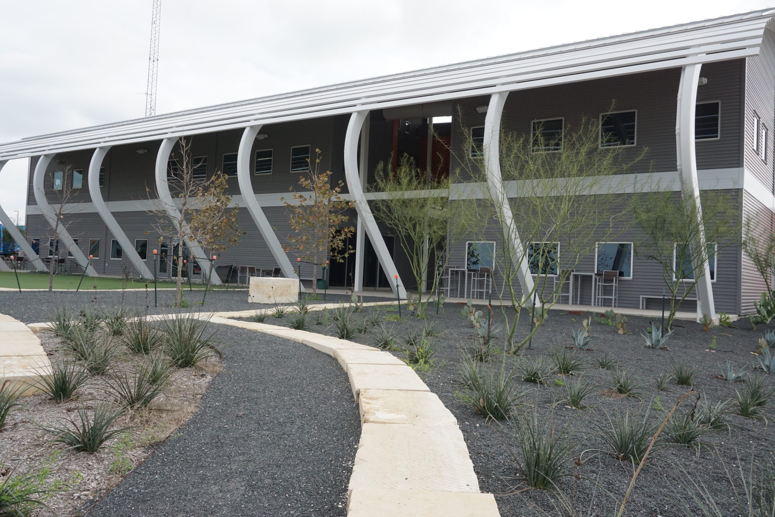 Modern building with curved white beams and landscaped pathway.