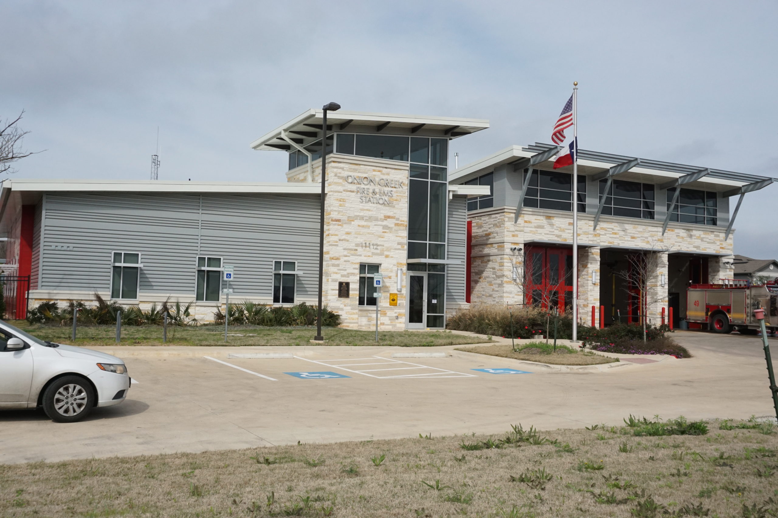 Modern fire station with fire trucks inside and American flag outside.